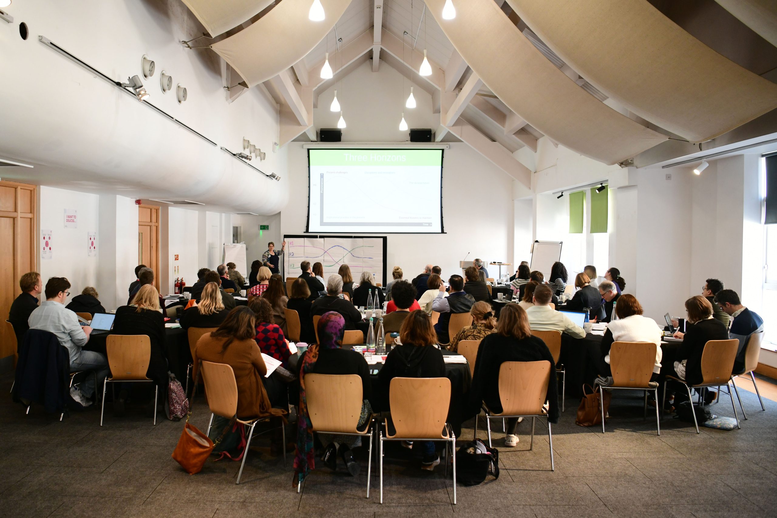 A group of people seated in a conference room listening to a presentation with slides projected at the front.